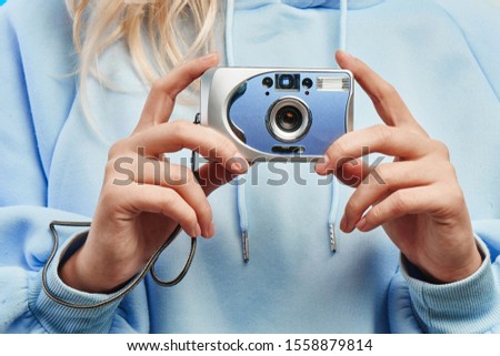 Female hands holding a vintage hipster film camera and take a picture, blue background