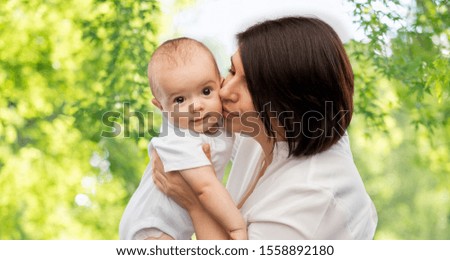 family, child and parenthood concept - happy smiling middle-aged mother kissing little baby daughter over green natural background
