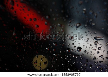 Rain drops accumulate on glass with blurred neon signs in background