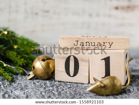 Chinese New Year 2020. Date January 1 on a wooden calendar with metal rat and christmas bell and twigs of a Christmas tree on agrey background. New Year of the rat.
