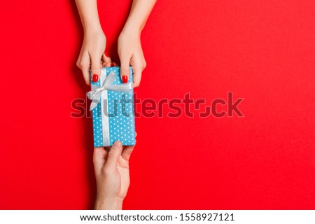 Top view of giving and receiving a gift on colorful background. Present in male and female hands. Love concept. Copy space.