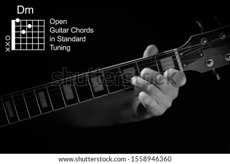 Open Guitar Chords in Standard Tuning guitar tutorial series. Closeup of hand playing Dm chord on guitar, on black background. Black and white photo.