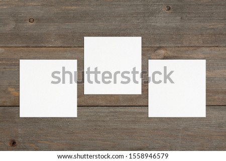 Three empty square white business cards mockup on brown rustic wooden background. Flat lay, top view. Uneven, open composition. Soft shadows. For branding identity, logo design pitches and marketing.