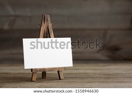 Standard sized empty white business card mockup with wooden easel on a brown rustic wooden surface. For branding identity, logo design pitches and marketing.