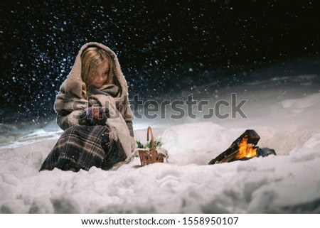 cute little girl sitting and warming herself by the fire in the winter evening. fantastic night by the fire. frame as illustration to a fairy tale