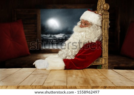 Red old Santa Claus and wooden table of free space for your decoration.Dark old window sill and moon on sky.Copy space and cold december time.Xmas pillows of red color on deck.