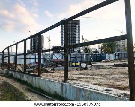 Inside view of a large industrial construction site behind a fence with tools, barrel pipes and building materials on which new houses are being built