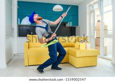 Funny male cleaning worker in special clothes playing with a mop as a guitar in the modern stylish kitchen. Cleaning services. Having fun at workplace.