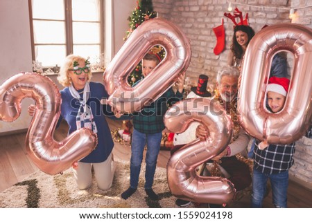 Beautiful happy family celebrating Christmas at home, having fun holding giant balloons shaped as numbers 2020, representing the upcoming New Year