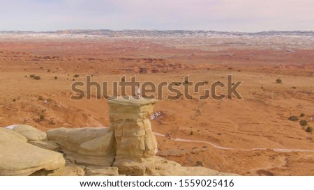 AERIAL: Woman stands on top of a boulder and takes photos of the breathtaking canyon in North America. Female photographer taking pictures of the stunning desert in Utah. Tourist girl photographing.