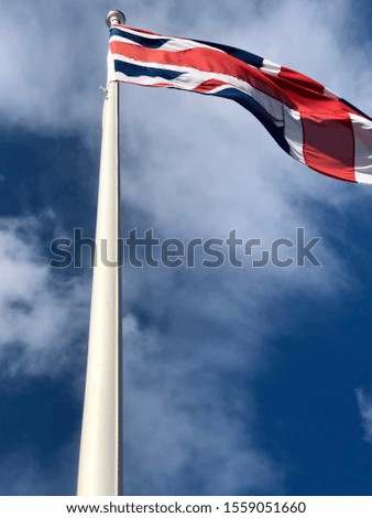 Union Jack blowing in the wind on a flag pole with clouds in the background