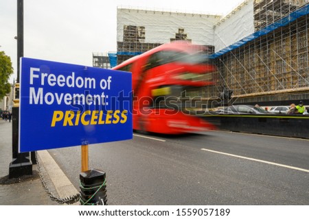 Red London bus with motion blur as it passes anti-Brexit Freedom of Movement sign outside The House of Parliament