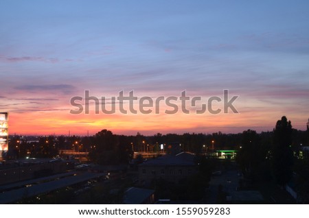 View of the dramatic sky above the sity at sunset with dark blue clouds and pink, purple and yellow flashes from the sun's rays Royalty-Free Stock Photo #1559059283
