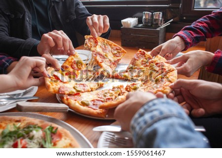 group of students friends eat Italian pizza, hands take slices of pizza in a restaurant, close-up Royalty-Free Stock Photo #1559061467