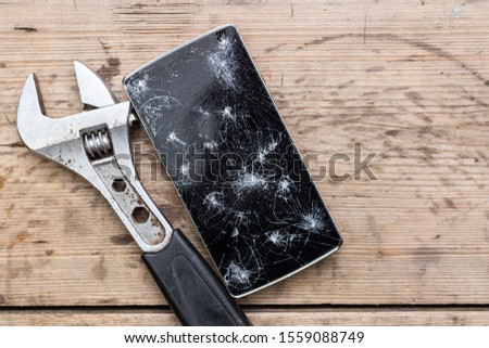 Smartphone repair concept. Crashed smartphone screen with grunge repairing tools on wooden background. A modern phone with smashed screen and bunch of 
instruments representing the concept of repair.