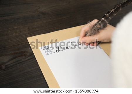 Child is writing a letter for Santa. Wood background. Close-up