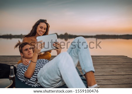 Young couple watching videos or sharing media content from a tablet, while spending time by the river
