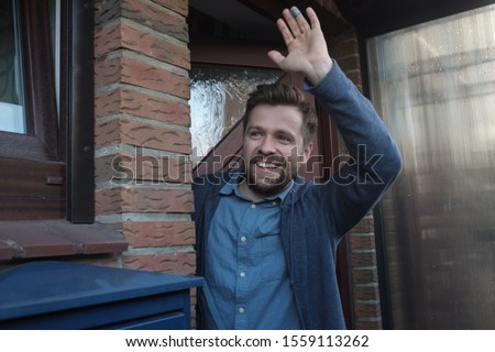Smiling young man waving with a friendly cheerful smile to his new neighbours. Royalty-Free Stock Photo #1559113262