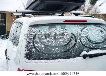 Children painted a smiling face on the snow-covered windows of the car. Family vacation during the winter holidays.
