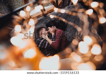 Lovers man and woman lie on the bed and kiss under a Christmas garland. Holidays, New Year, family vacation, romantic dating.