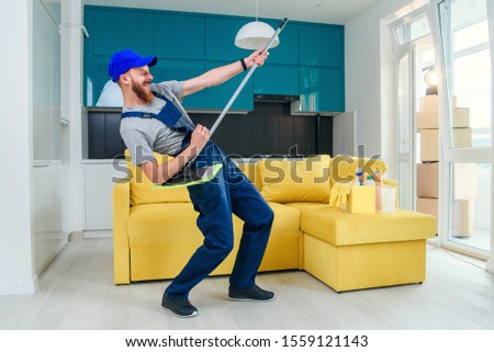 Funny picture of male cleaning worker in special clothes playing with a mop as a guitar in the kitchen