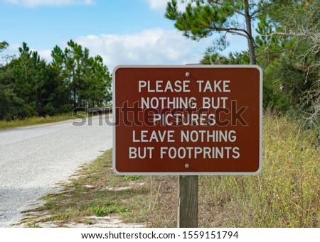 Brown sign with "Please take nothing but pictures. Leave nothing but footprints" alongside a road.