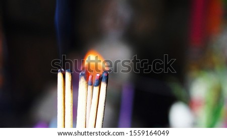 incense sticks lit in a Buddhist temple, from them comes a slight smoke. they smolder people pray
