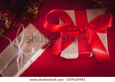 New Year's gift with a red ribbon in craft brown paper. Christmas composition of cones, tinsel and gifts on a red background.