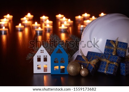 White construction hard hat, candles, gift boxes, fir branch and Christmas ornament on black background. Construction New Year, Christmas background. For greeting card or advertising