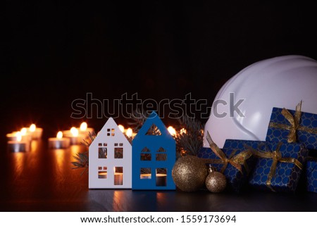 White construction hard hat, candles, gift boxes, fir branch and Christmas ornament on black background. Construction New Year, Christmas background with copy space. For greeting card or advertising