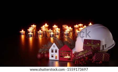White construction hard hat, candles, gift boxes, fir branch and Christmas ornament on black background. Construction New Year, Christmas background with copy space. For greeting card or advertising
