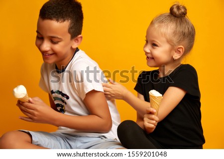 Cute little boy doesn't want to share ice cream with his sister. studio shot on a yellow background