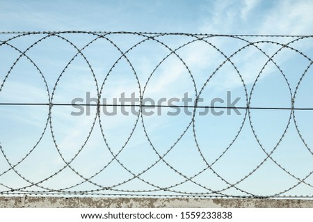 Barbed wire stretched on the fence to protect the territory and the border against the blue sky