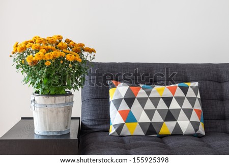 Bright cushion on a sofa, and orange chrysanthemums on a side table. Royalty-Free Stock Photo #155925398