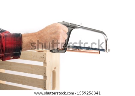 a plumber in a red shirt using a hack saw to cut a piece of copper pipe isolated on white