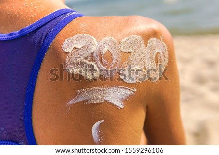  Christmas time spent at the beach in summer. Young woman wearing bikini with sunlotion 2020 on a shoulder