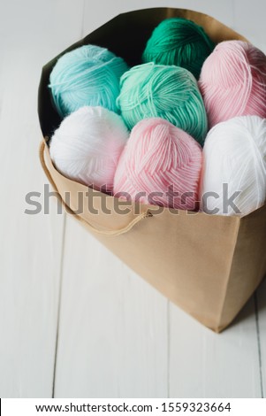 oval acrylic colorful wool yarn thread skeins lying in kraft paper brown package on white wooden boards background, top view of vertical stock photo image