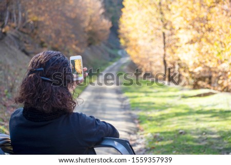 Backside view of a young woman taking picture with smartphone during autumn season in rural area 