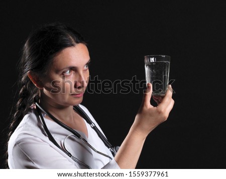 A female doctor holds a glass of water and medicine and poses emotionally on a black background
A female doctor in holding a glass of water and medicine posing on a black background. Doctor template.