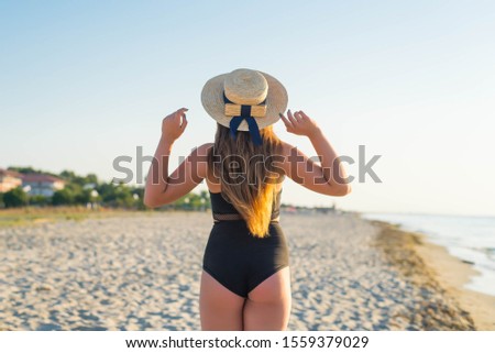 Back of cheerful plus size teenage girl wearing hat enjoying the beach. smiling, happy, positive emotion, summer style.