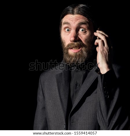 strange bearded senior priest with a smartphone, bearded old man is calling on a dark background