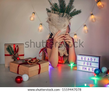 Cute small girl in red Santa hat waiting for miracle before Christmas season, festive illumination, garland and packed gifts, she is ready for celebration, indoor portrait over white background