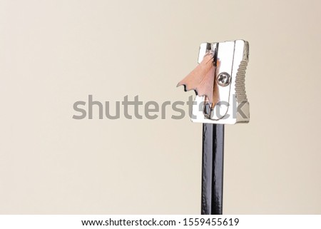 A sharpener is put on a pencil. Wooden pencil shavings come out of the sharpener. Minimalism, light background. Creative office concept. Place for text.
