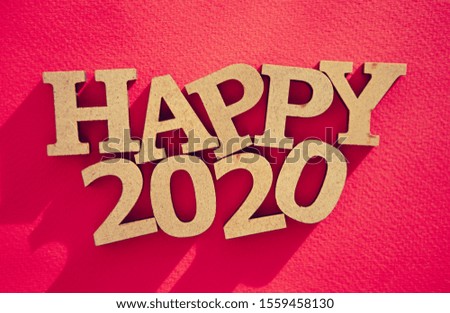 Happy 2020 background.Red paper backdrop,rustic wooden letters in flat lay style shot from above.Winter holiday wallpaper with vibrant colors