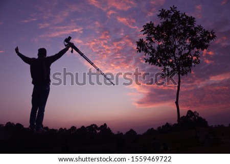 Photographer taking pictures outdoors, silhouette of a man with camera over sunset background, 