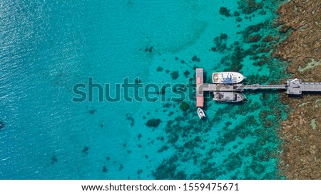 2 motor yachts lined up each side of a jetty in tropical island over a reef and turquoise water with rocky outcrop.  Aerial shot from above. Fiji island Kokomo luxury resort. South Pacific