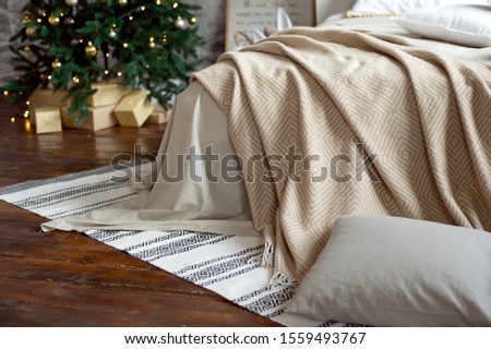 Christmas apartment decor, Scandinavian cozy home decor, bed with warm knitted blankets next to the Christmas tree. Lights and garlands