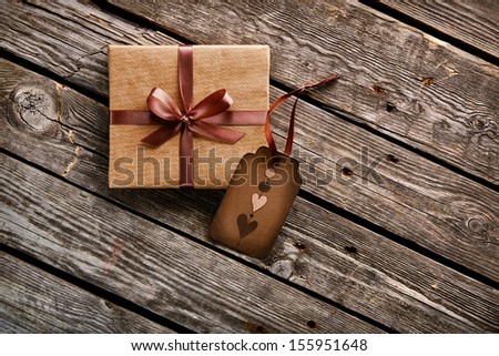 Vintage gift box with gift tag with hearts on old wooden background.