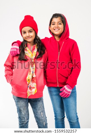 Two Indian little girls in warm cloths standing against white background