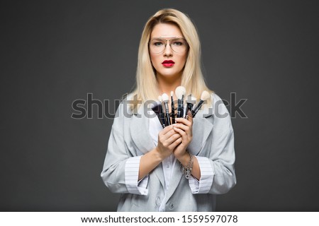 girl makeup artist in a blouse and a jacket holds makeup brushes in her hand, isolated on gray background.